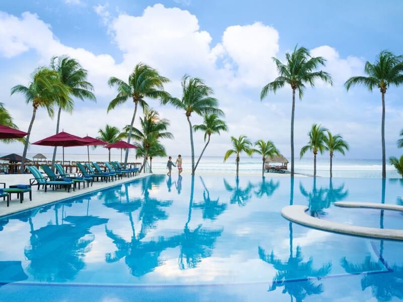 Großer Pool mit Palmen und roten Sonnenschirmen